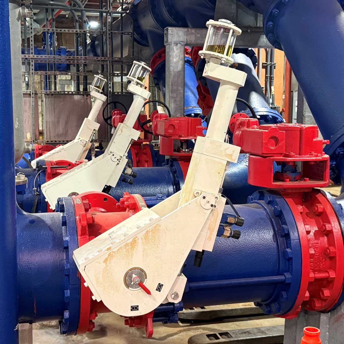 Large triple offset (TOV) check valves with progressive sealing system and adjustable proprietary dampening system for pump protection in wastewater, along with corresponding gear-operated TOV isolation valves.